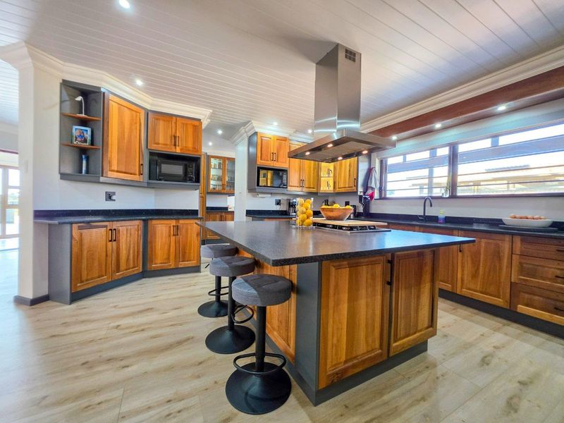 Modern kitchen featuring wooden cabinetry, stone countertops, a central island with an integrated cooktop, and a stainless steel extractor fan.