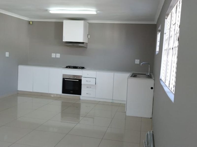 A clean, empty kitchen featuring white cabinetry, built-in oven and hob, extractor fan, and neutral tiled flooring.