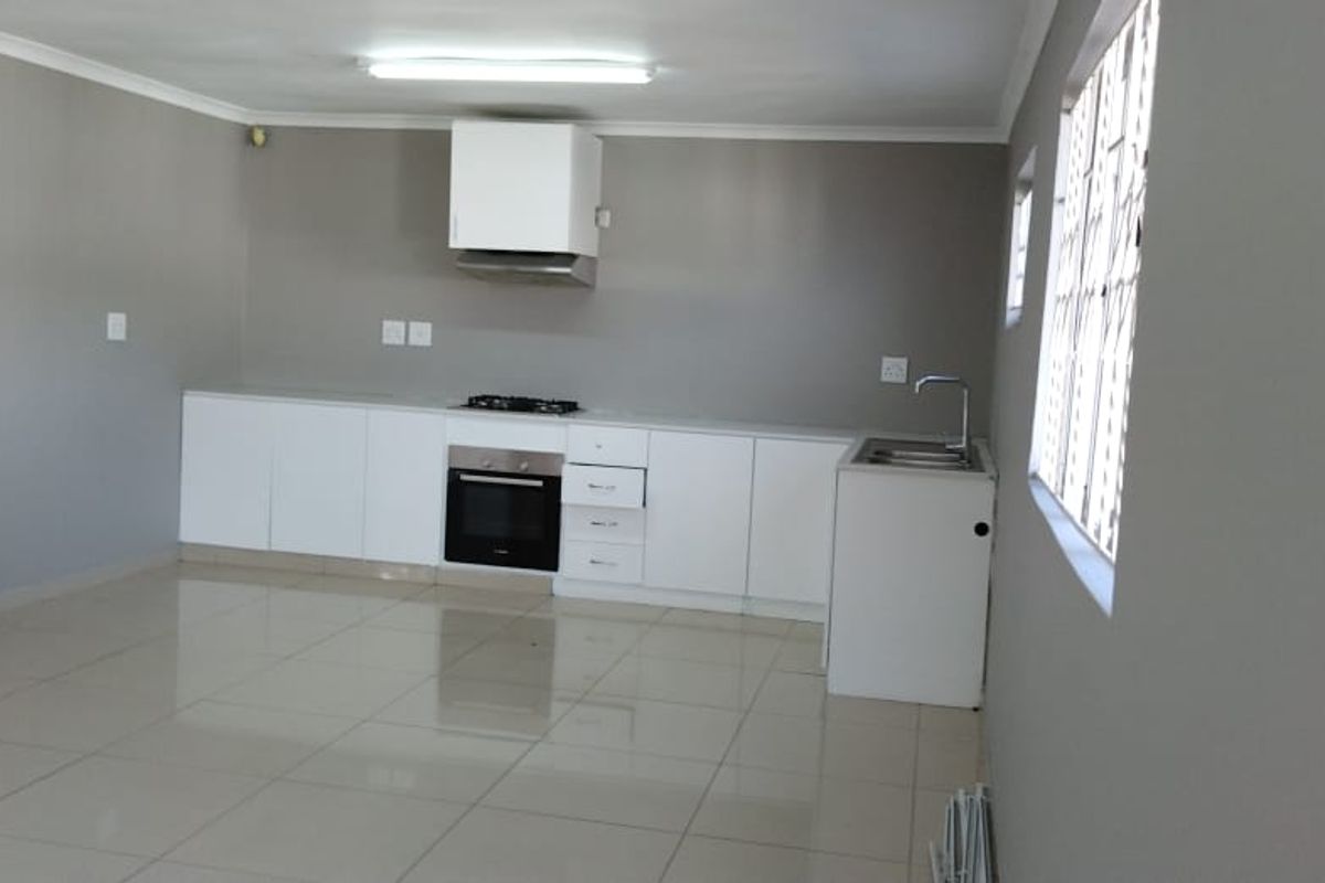 A clean, empty kitchen featuring white cabinetry, built-in oven and hob, extractor fan, and neutral tiled flooring.