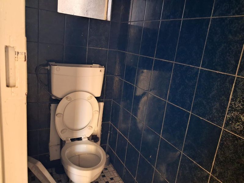 A small bathroom featuring dark blue wall tiles and mosaic floor tiling, currently requiring renovation and modernization of fixtures.