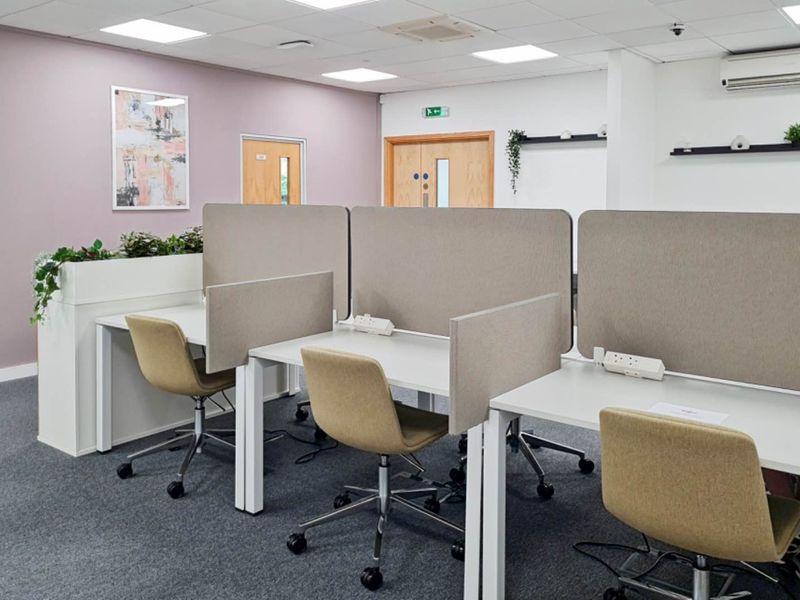 A modern, well-maintained office space featuring carpeted flooring, suspended ceilings with recessed lighting, and integrated desk partitions with built-in power connectivity.