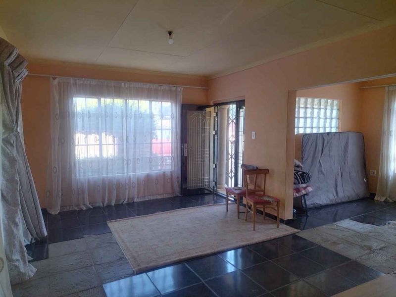A living room area featuring dark tiled flooring, a glass block feature window, and direct access to the exterior through a security gate.