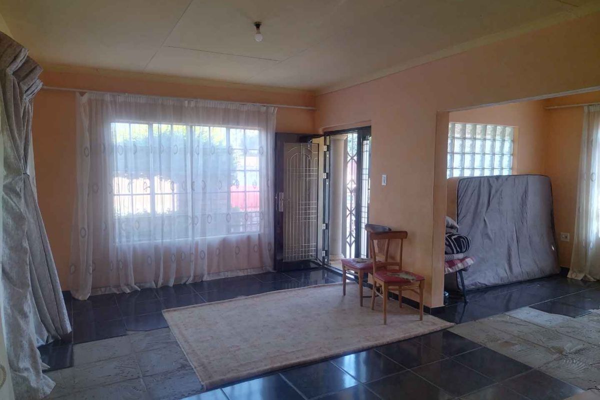 A living room area featuring dark tiled flooring, a glass block feature window, and direct access to the exterior through a security gate.