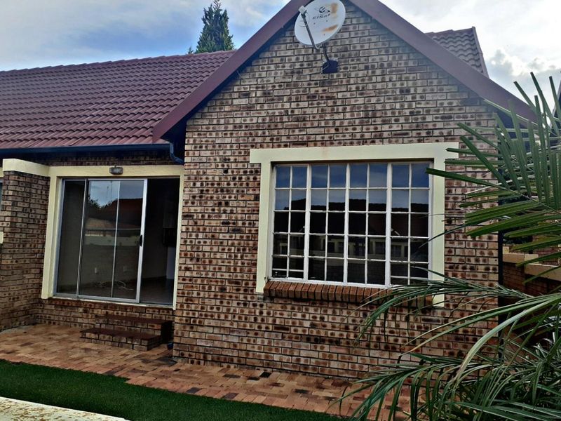 Rear exterior view of the townhouse featuring face brick construction, a tiled roof, a paved patio area, and a sliding glass door entrance.
