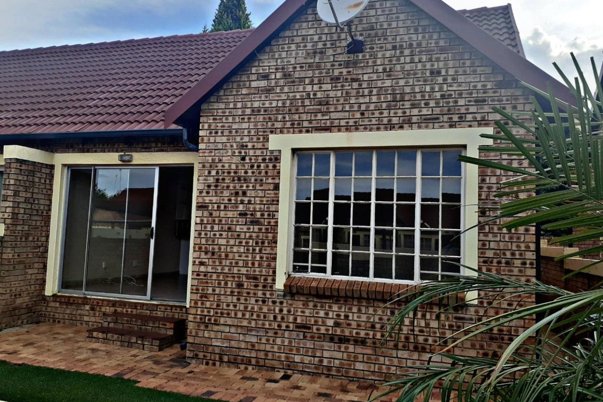 Rear exterior view of the townhouse featuring face brick construction, a tiled roof, a paved patio area, and a sliding glass door entrance.