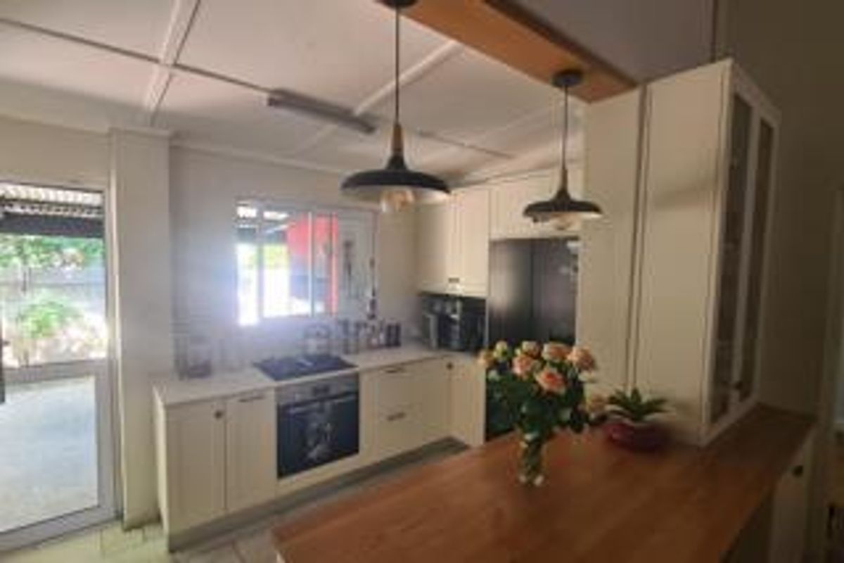 A functional kitchen featuring cream cabinetry, a built-in oven, a cooktop, and a wooden breakfast bar, with direct access to the outdoor area.