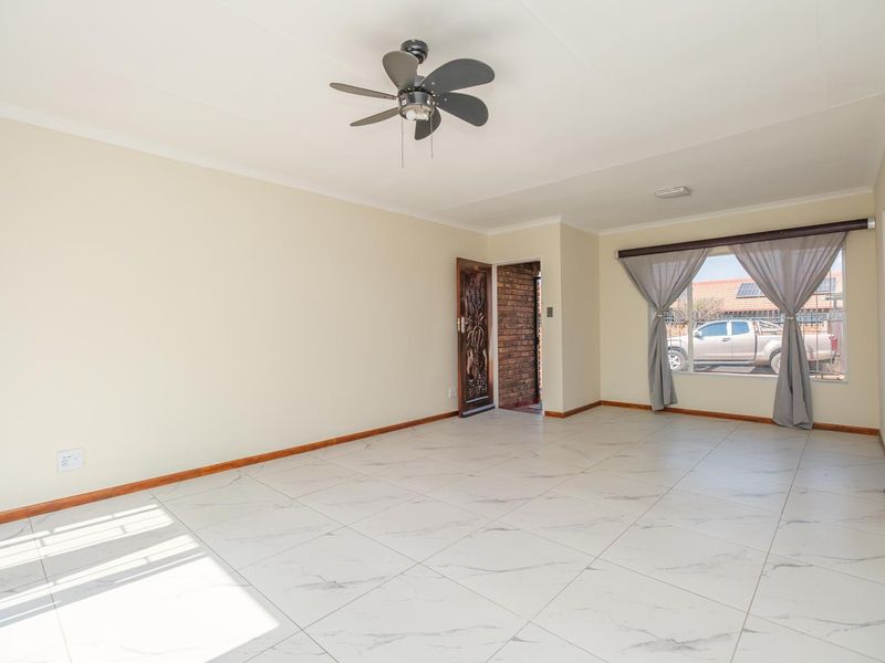 A bright, empty living room featuring modern marble-look floor tiles, a ceiling fan, and a wooden entrance door.