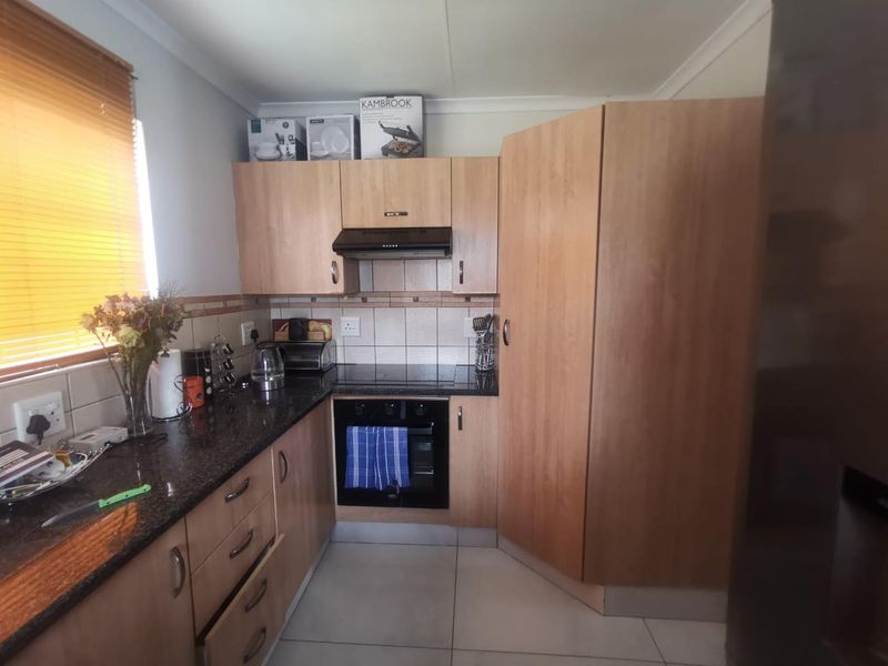 A functional kitchen featuring light wood cabinetry, granite countertops, a built-in oven, and an electric hob with an extractor fan.