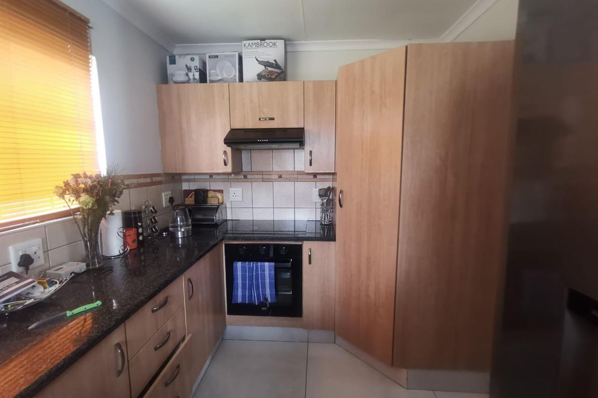 A functional kitchen featuring light wood cabinetry, granite countertops, a built-in oven, and an electric hob with an extractor fan.