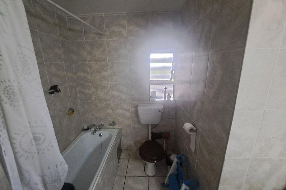 A functional bathroom featuring full-height wall tiling, a standard bathtub with shower attachment, and a toilet.