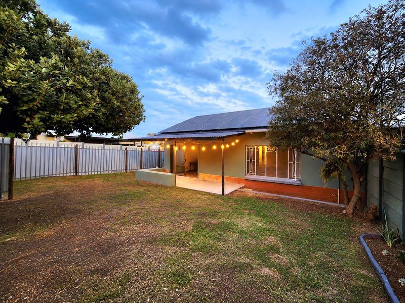 Rear view of the house featuring a covered patio, solar panel installation on the roof, and a private garden area with perimeter fencing.