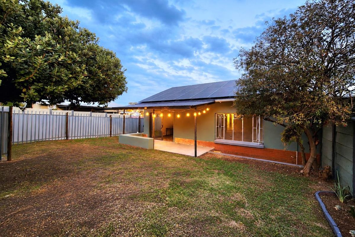 Rear view of the house featuring a covered patio, solar panel installation on the roof, and a private garden area with perimeter fencing.