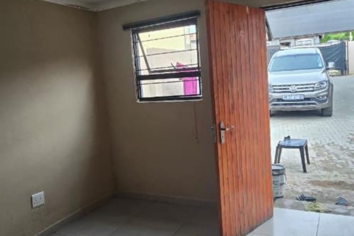 An empty, tiled living area featuring a timber door, steel window frame, and recessed ceiling lighting, offering a blank canvas for interior design.