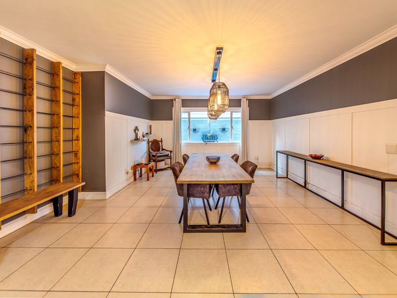 Spacious dining room featuring elegant wainscoting, crown molding, tiled flooring, and custom built-in wall shelving, creating a sophisticated and well-defined entertaining space.