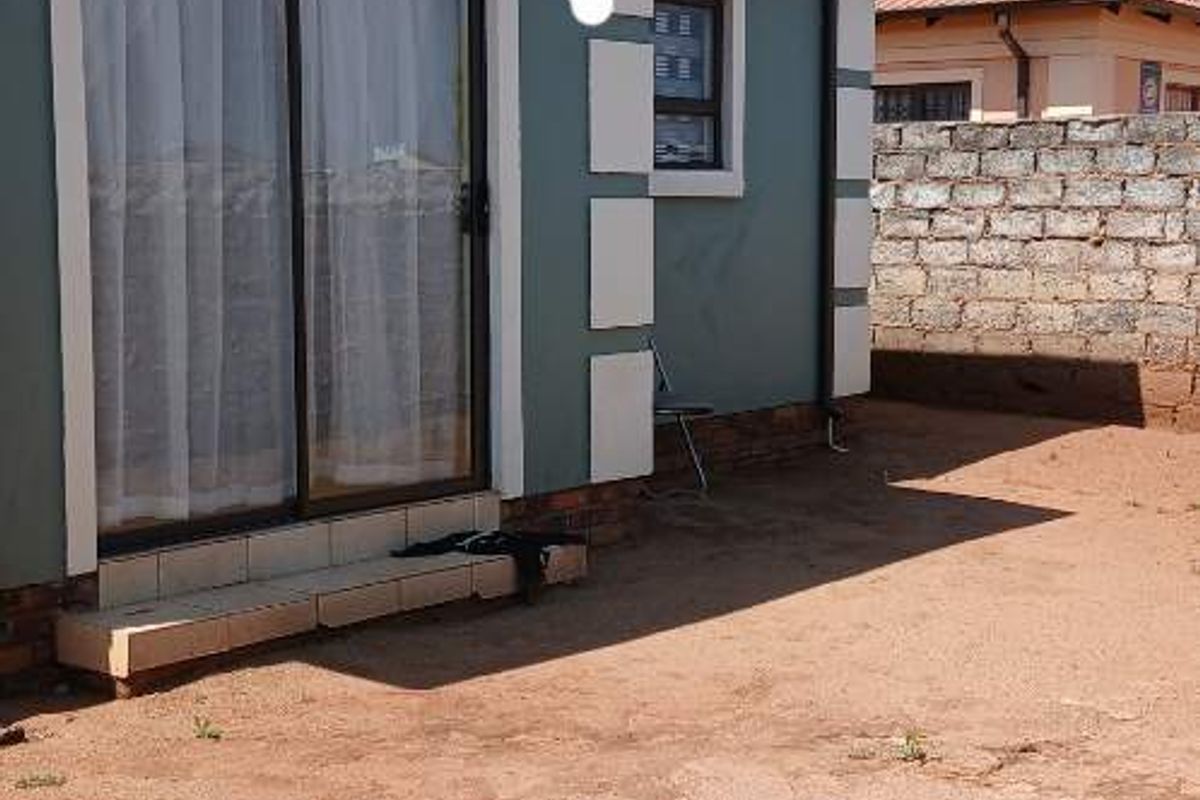 Rear view of the house featuring a sliding glass door, tiled roof, and an expansive unlandscaped yard area enclosed by a concrete block boundary wall.