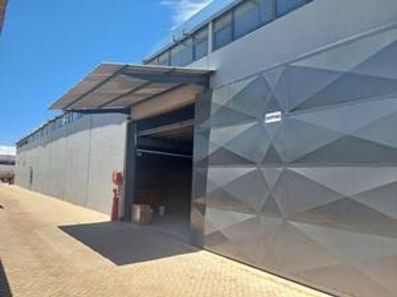 Industrial property exterior featuring a large geometric patterned roller shutter door, metal canopy, and paved access area.