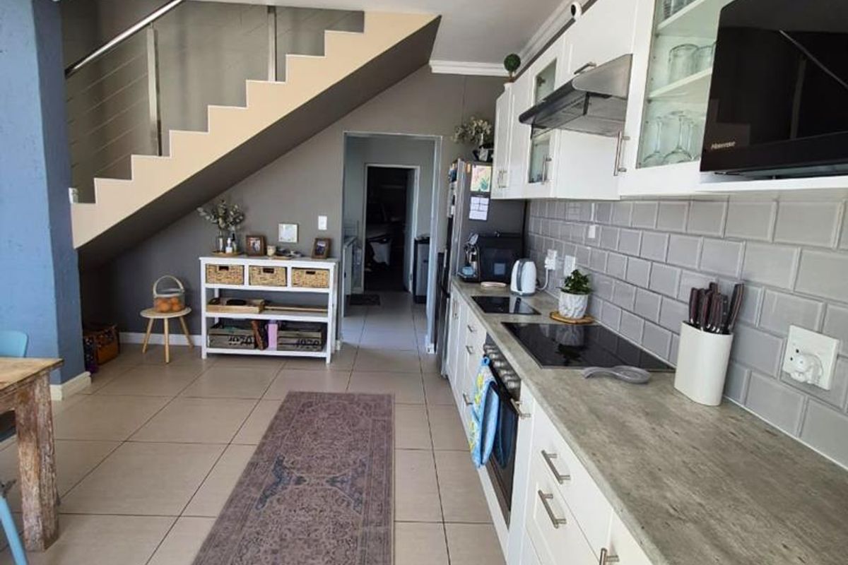 Modern kitchen featuring white cabinetry, subway tile backsplash, and integrated appliances, seamlessly flowing into an open-plan living area with a staircase.