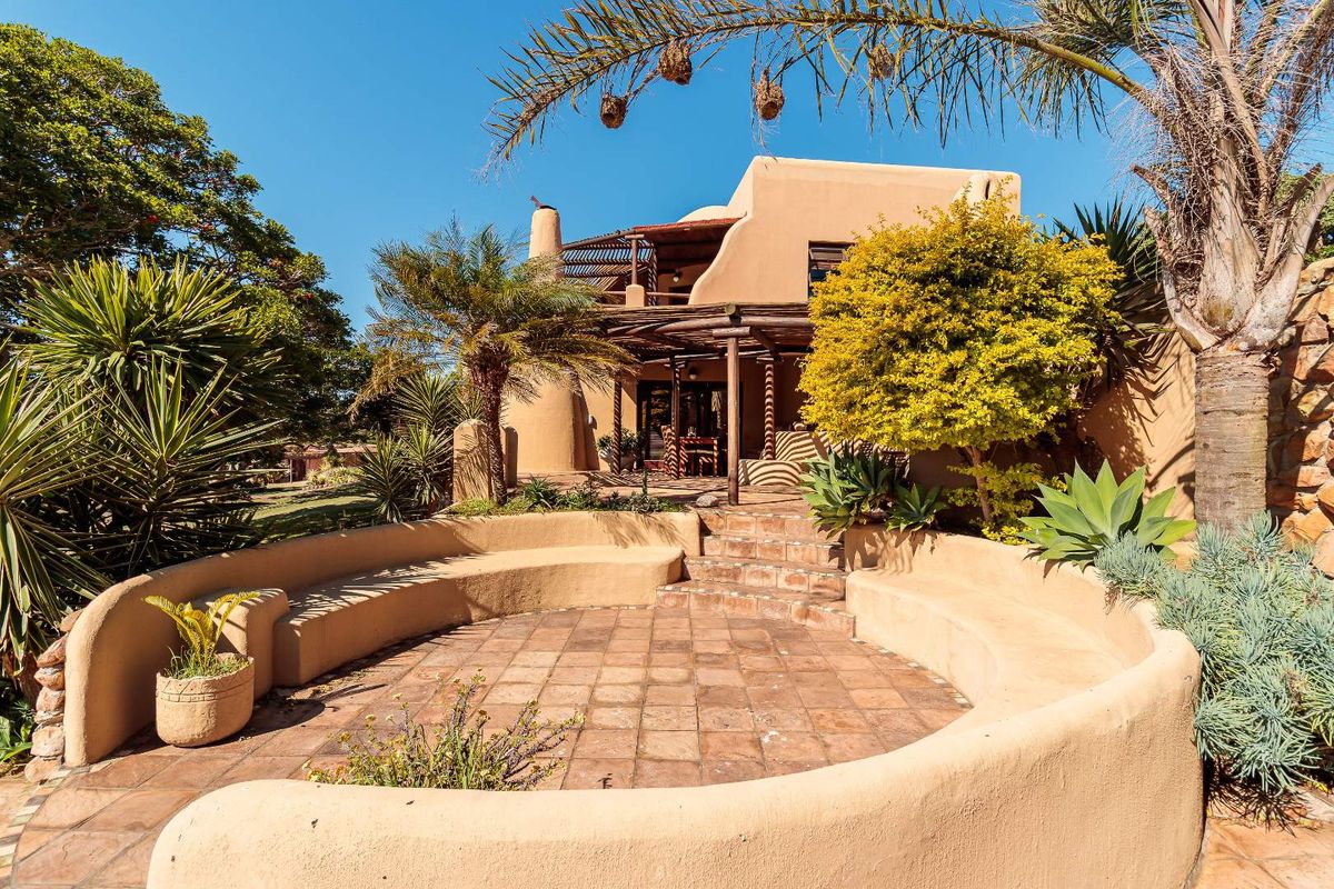 A charming rear exterior view featuring a terracotta tiled patio with built-in curved seating, a timber pergola, and established garden landscaping.
