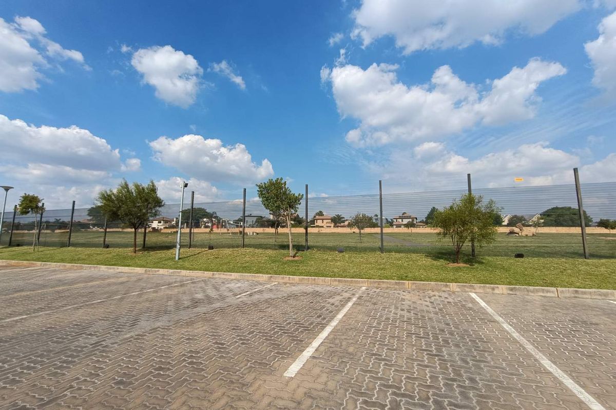 A view of the paved parking area adjacent to a well-maintained communal green space and security fencing.