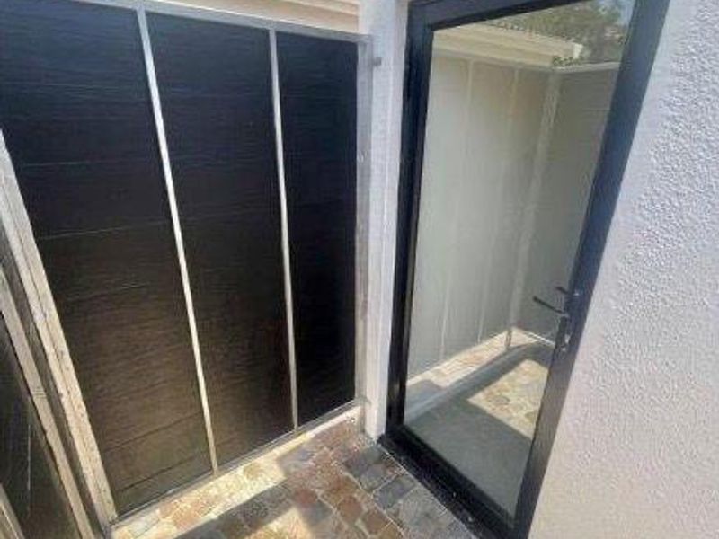 A private exterior courtyard featuring stone paving, a modern black-framed glass door, and a privacy screen against a textured white wall.