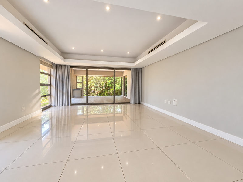 Spacious, light-filled living area featuring polished porcelain tiles, recessed ceiling lighting, ducted air conditioning, and large sliding doors opening to an outdoor patio.