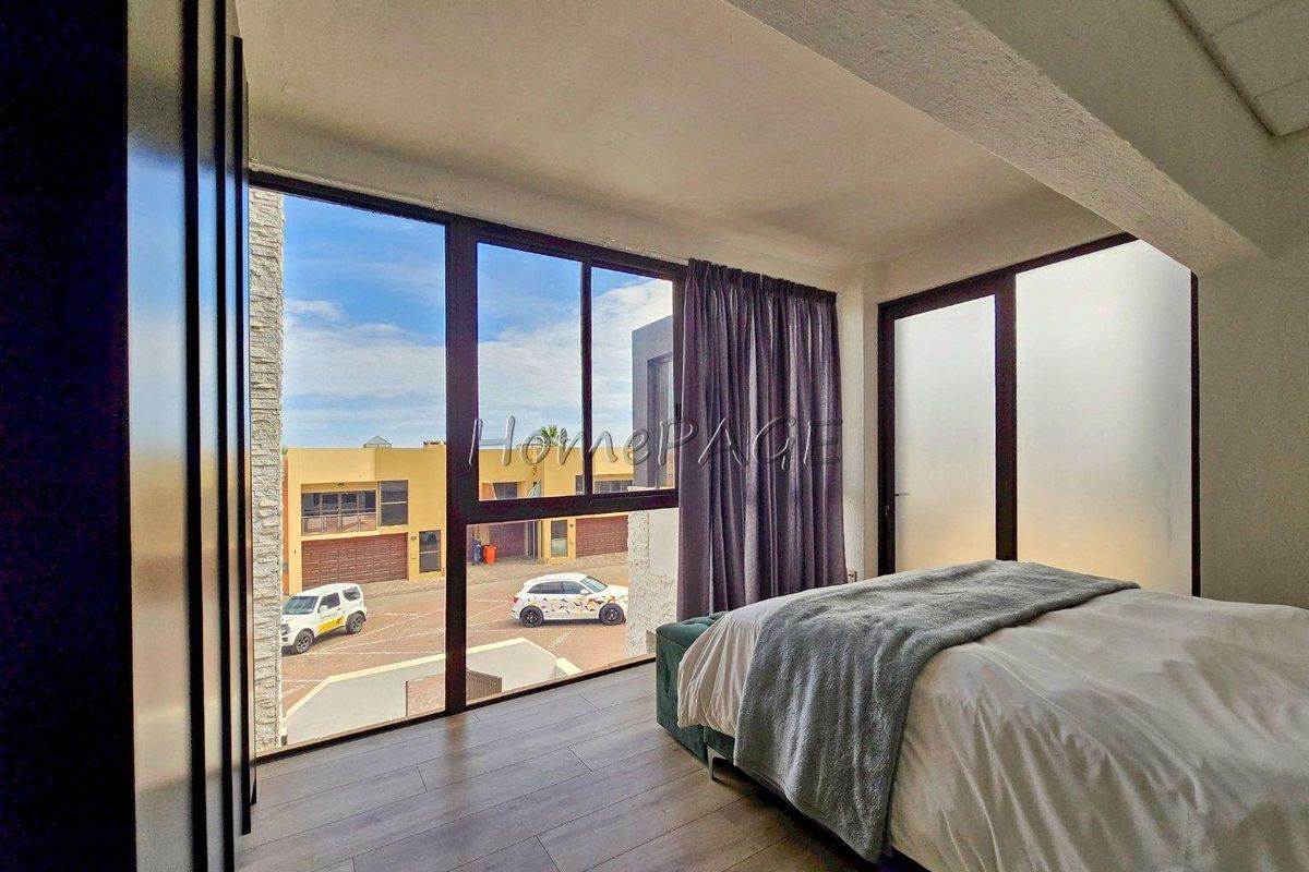 A bright bedroom featuring large floor-to-ceiling windows with views of the surrounding neighborhood and modern wood-look flooring.