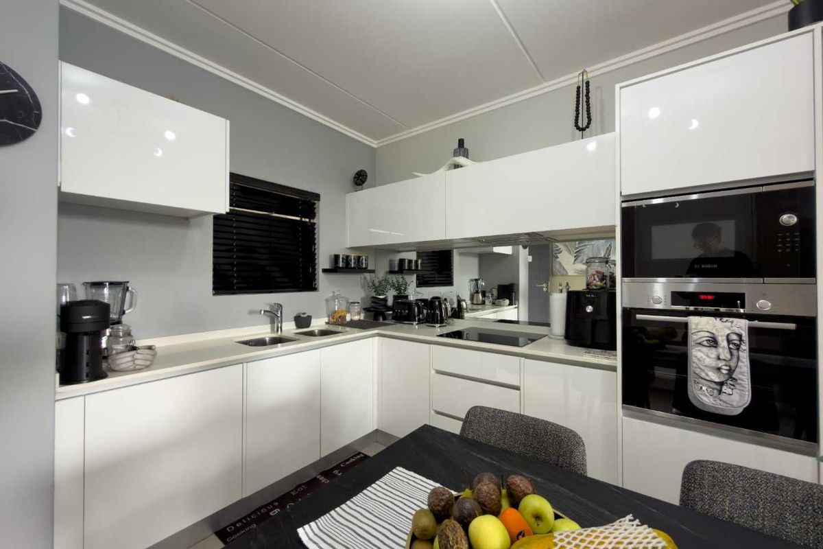Modern kitchen featuring sleek white cabinetry, integrated oven and microwave, and a functional L-shaped countertop layout.