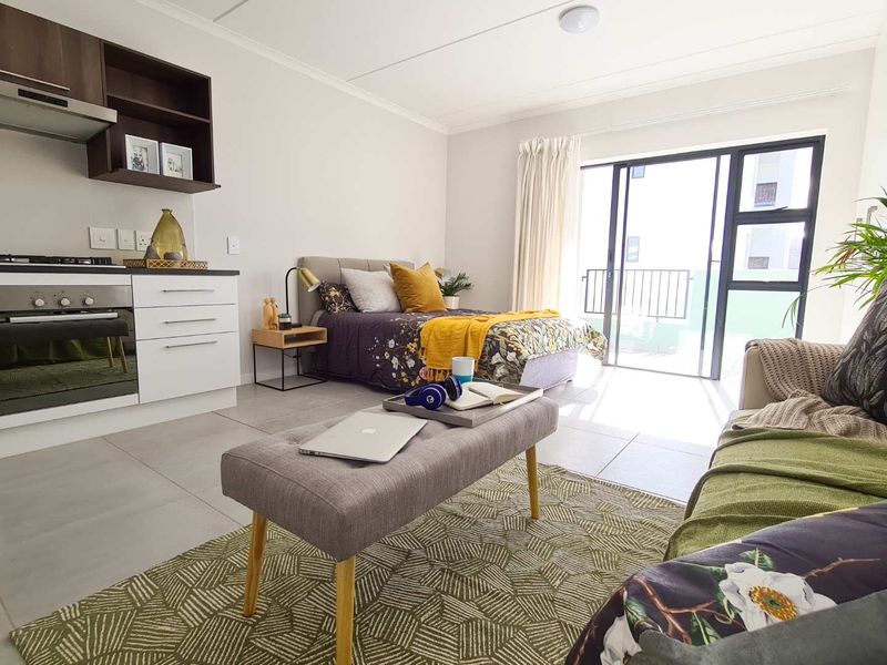 Modern open-plan studio apartment featuring a compact kitchen with built-in appliances, tiled flooring, and direct access to a private balcony through sliding glass doors.