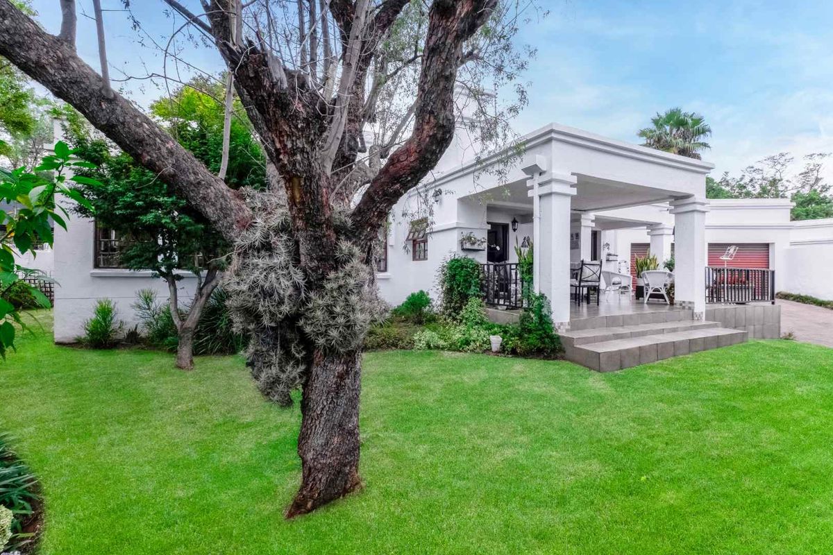 A well-maintained rear exterior view featuring a covered patio, tiled steps, wrought iron railings, and a lush green garden.