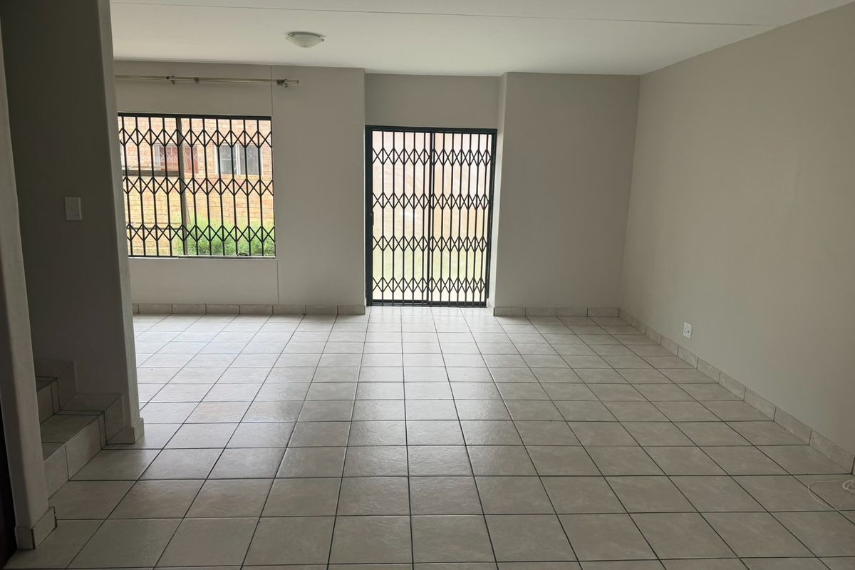 An empty, open-plan living area featuring neutral ceramic floor tiles, security gates on the sliding door, and security bars on the windows.