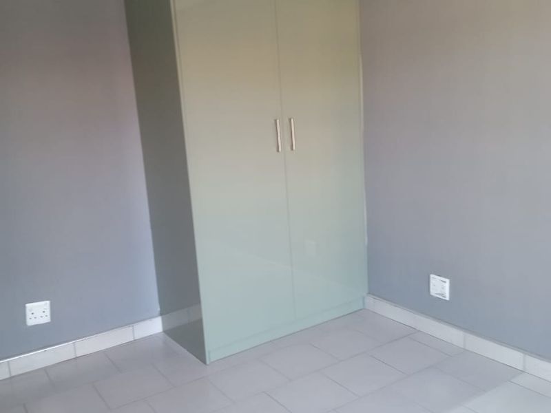 A clean, empty bedroom featuring neutral grey walls, light-colored tiled flooring, and a modern built-in wardrobe with a soft green finish.