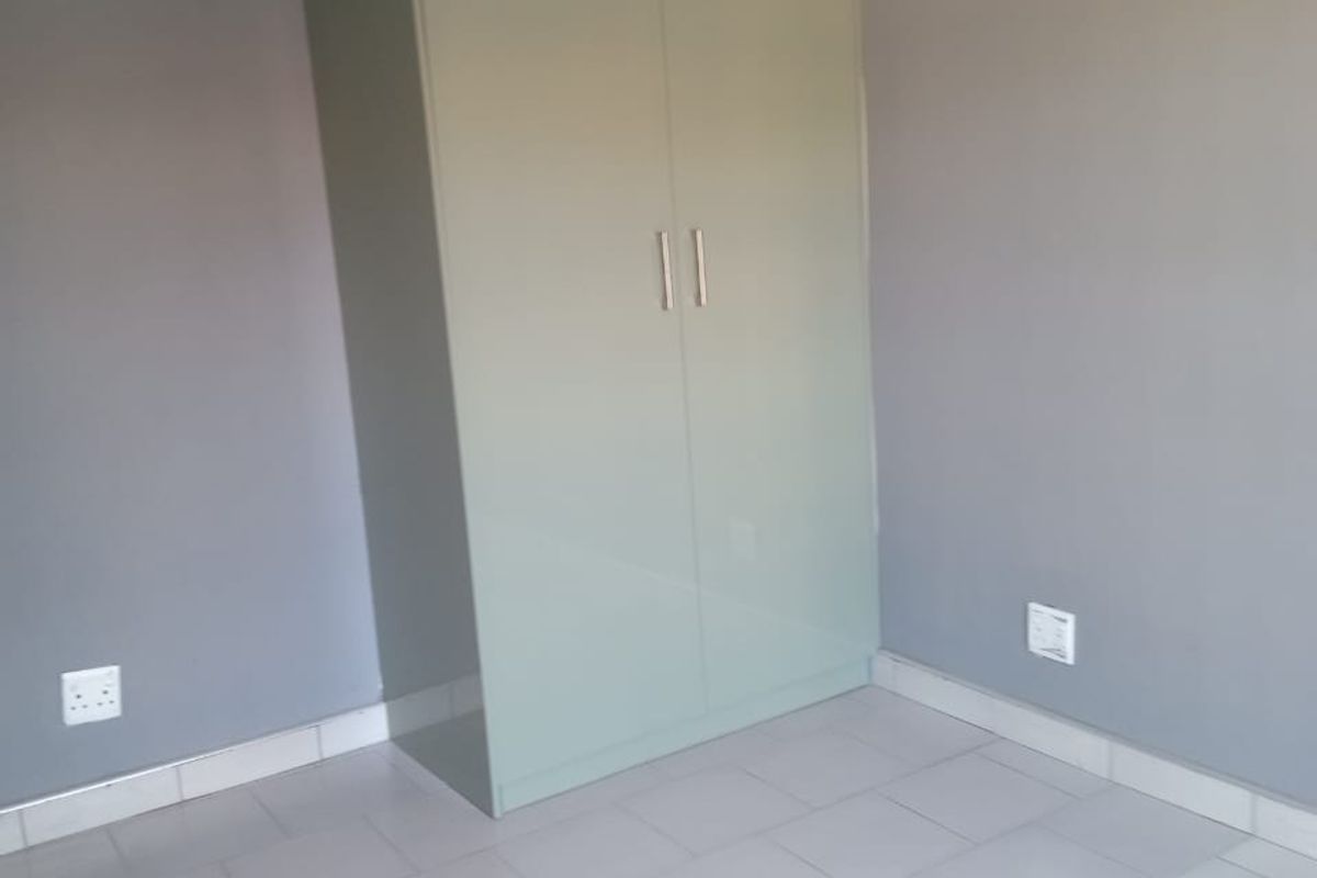 A clean, empty bedroom featuring neutral grey walls, light-colored tiled flooring, and a modern built-in wardrobe with a soft green finish.