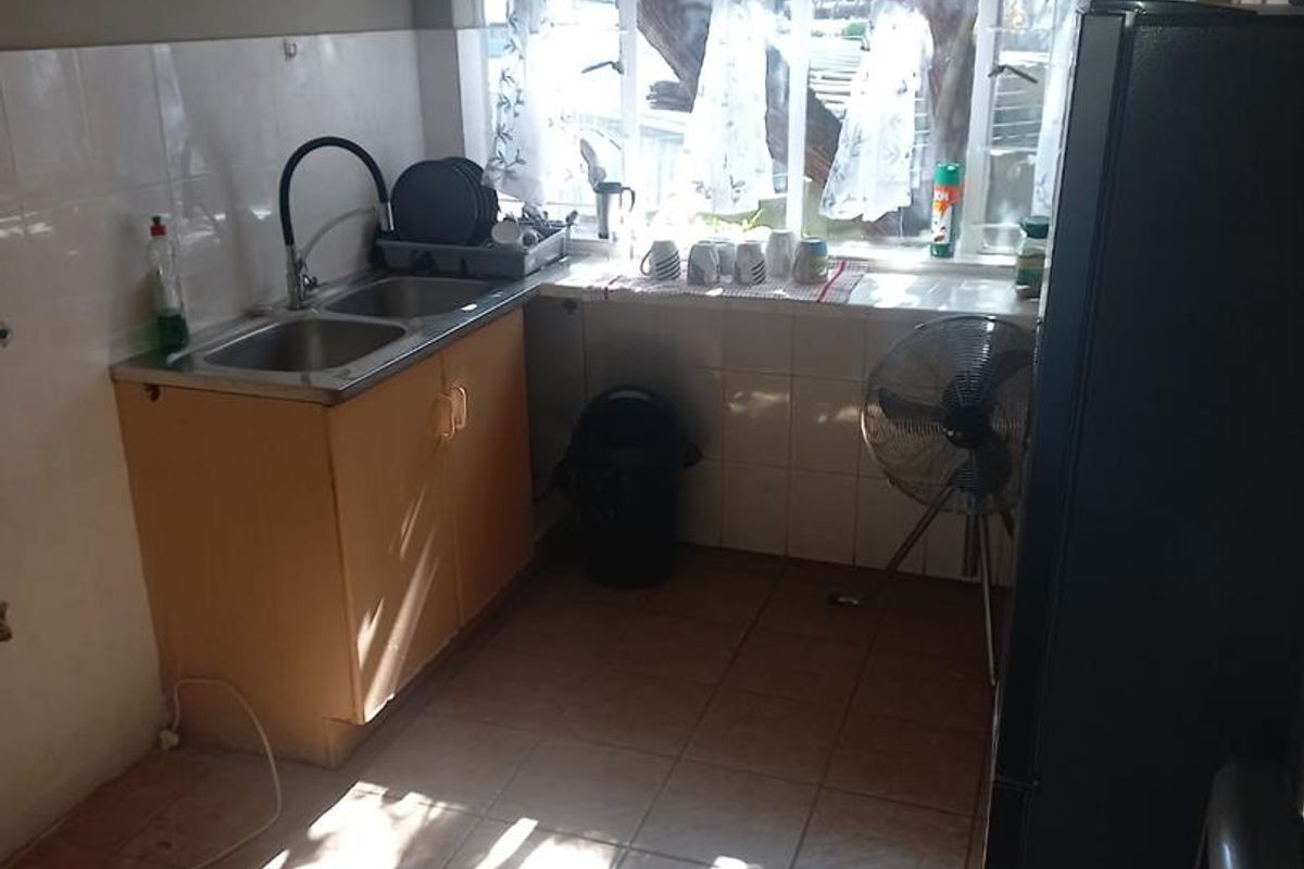 A compact kitchen area featuring a double sink, tiled splashbacks, and tiled flooring, with natural light provided by a large window.
