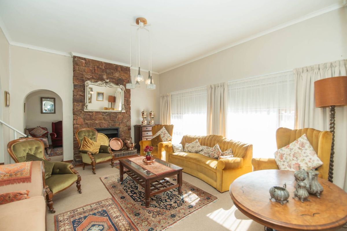 A spacious living room featuring a prominent stone fireplace, arched doorway, and large windows allowing for ample natural light.