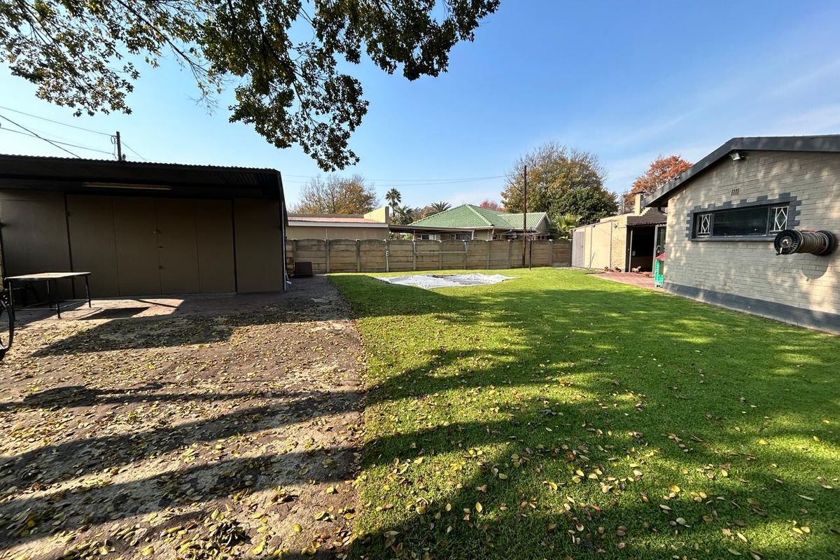 A spacious backyard featuring a large lawn area, a detached garage structure, and perimeter fencing, offering potential for outdoor landscaping and recreation.