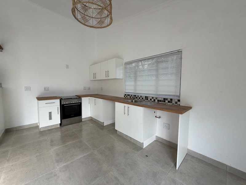 A clean, modern kitchen featuring white cabinetry, wooden countertops, a stainless steel sink, and a freestanding oven, with tiled flooring throughout.