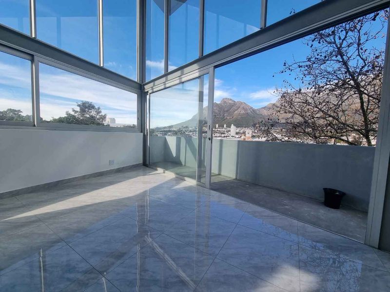 A bright, modern enclosed balcony featuring floor-to-ceiling glass walls, polished tile flooring, and expansive mountain and city views.