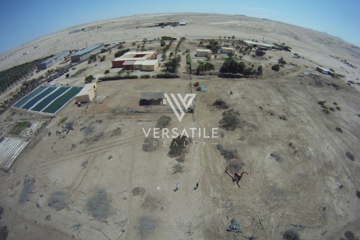 Aerial view of a large small holding property featuring multiple structures, open land, and water storage facilities in a desert landscape.