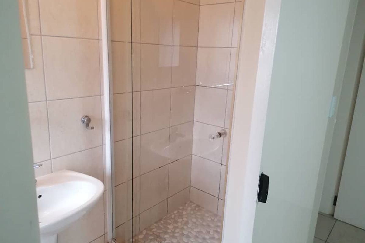 A functional bathroom featuring a pedestal sink and a glass-enclosed shower with pebble-style floor tiling and neutral wall tiles.