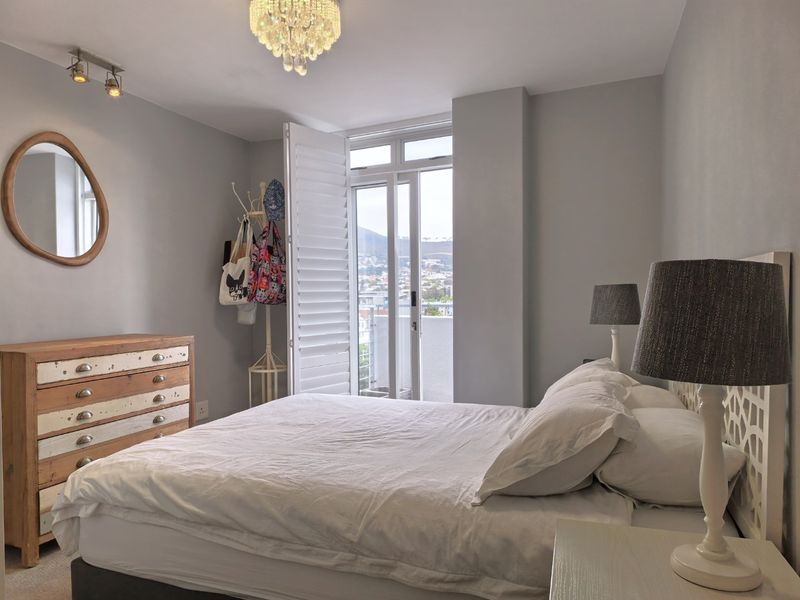 A well-maintained bedroom featuring plantation shutters, track lighting, and direct access to a private balcony with scenic views.