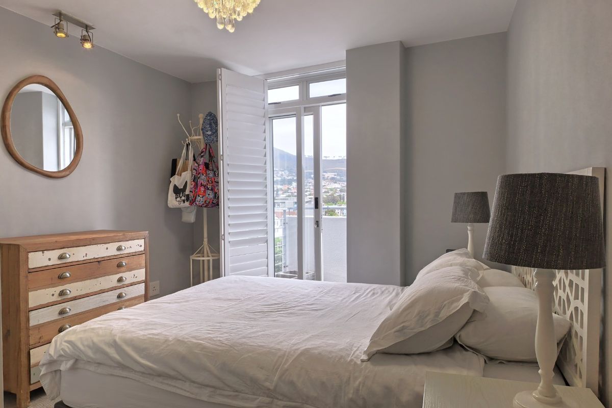 A well-maintained bedroom featuring plantation shutters, track lighting, and direct access to a private balcony with scenic views.
