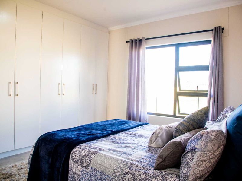 A well-maintained bedroom featuring floor-to-ceiling built-in cupboards and a large window providing natural light.