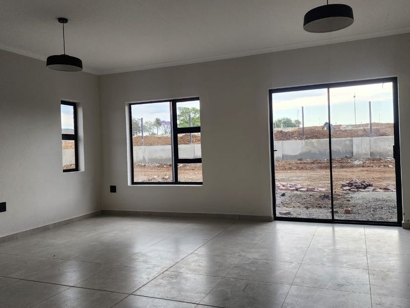 A bright, empty living area featuring modern tiled floors, large aluminium-framed windows, and a sliding glass door providing access to the exterior.