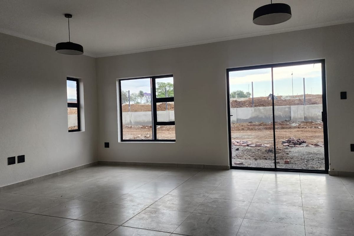 A bright, empty living area featuring modern tiled floors, large aluminium-framed windows, and a sliding glass door providing access to the exterior.