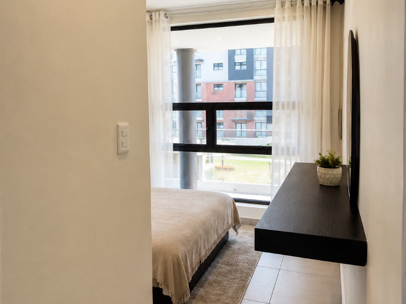 A bright bedroom featuring tiled flooring, recessed downlighting, and a large window with views of the surrounding complex.