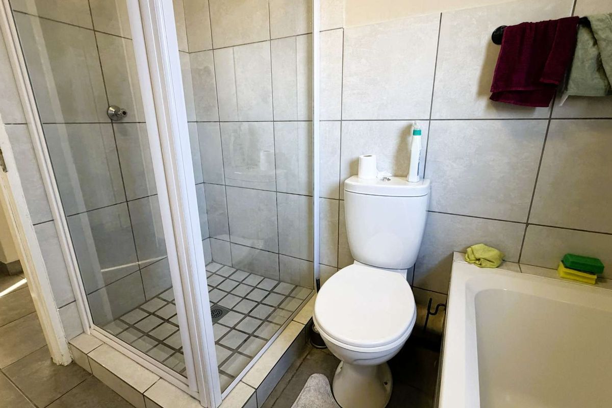 A functional bathroom featuring a glass-enclosed shower, a standard white toilet, and a bathtub with neutral wall tiling.