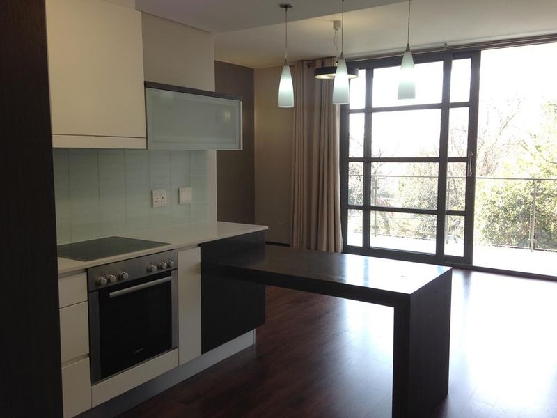 Modern open-plan kitchen featuring sleek cabinetry, built-in appliances, and a breakfast bar, flowing seamlessly to a balcony with large glass sliding doors.