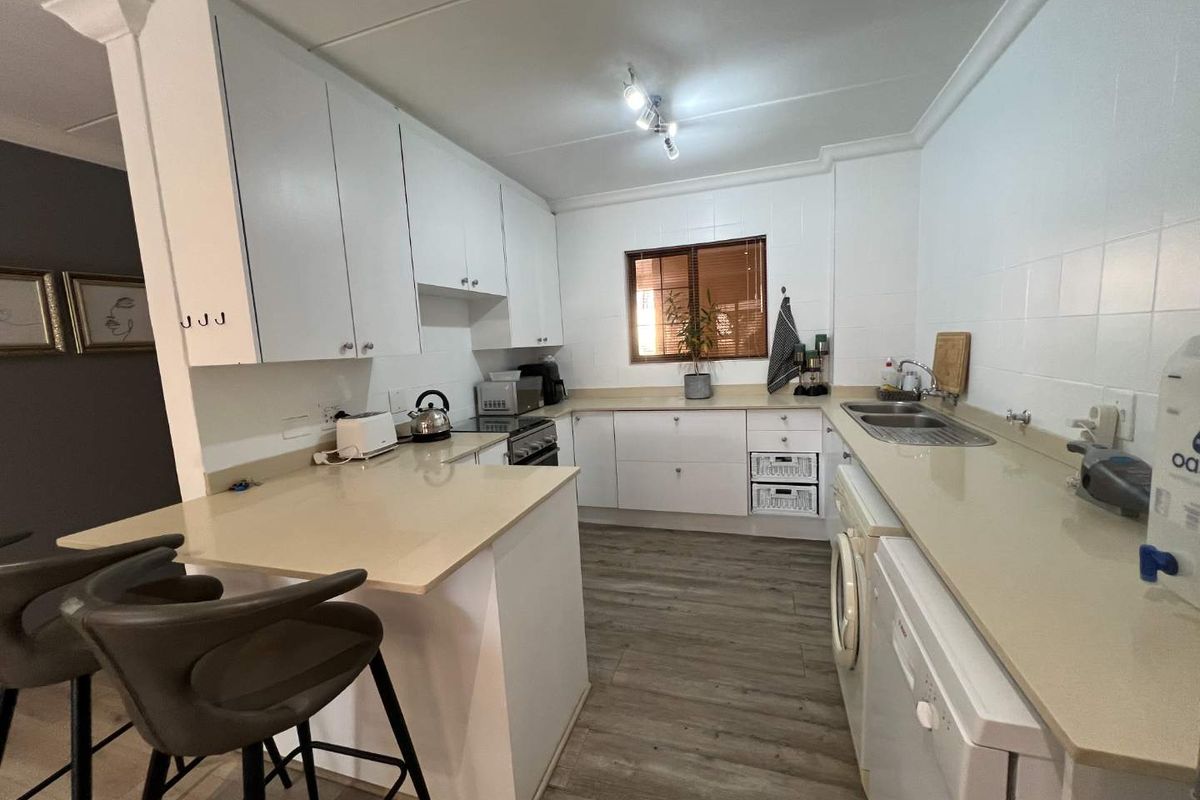 A functional kitchen featuring white cabinetry, stone-look countertops, integrated laundry appliances, and a breakfast bar peninsula.