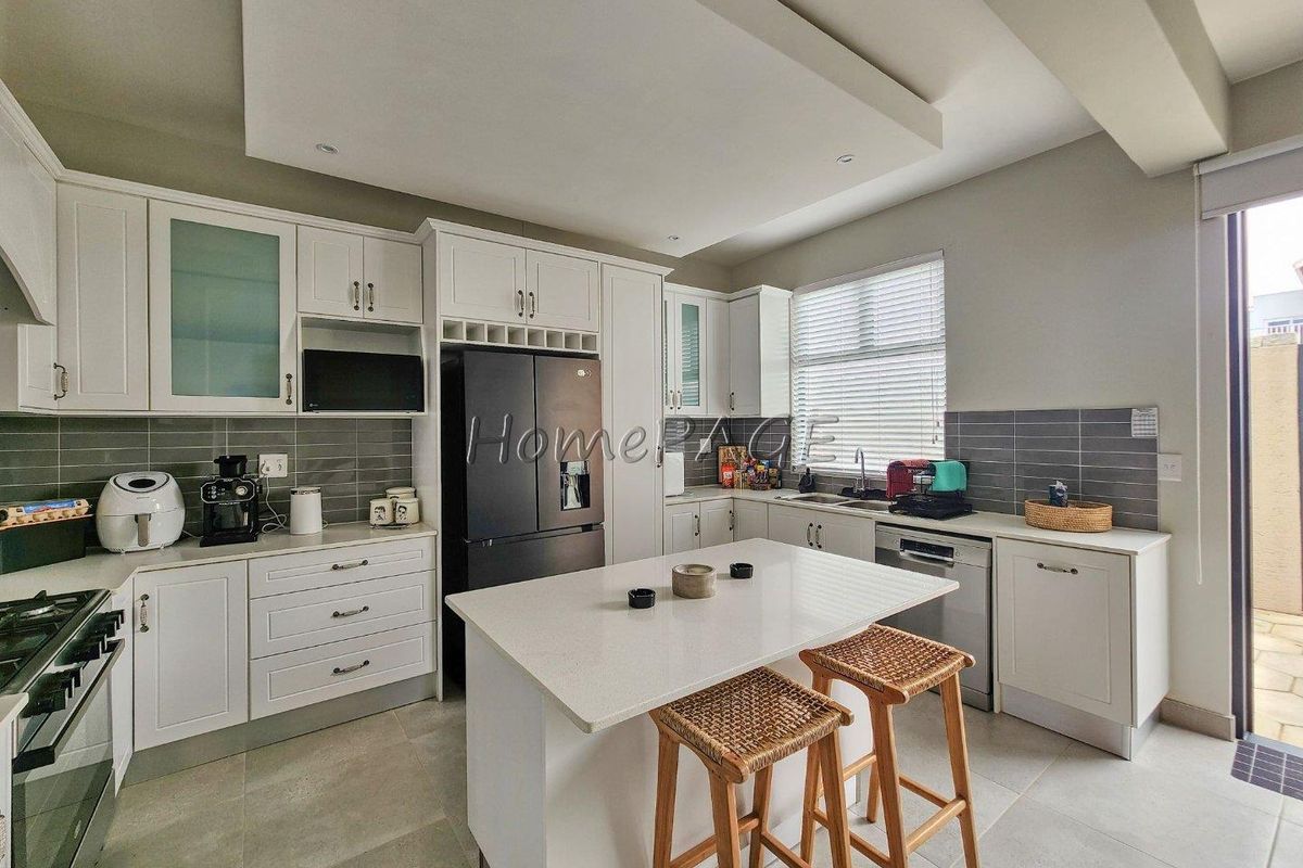 Modern kitchen featuring white cabinetry, stone countertops, a central island, tiled backsplash, and integrated appliances, with direct access to an outdoor patio area.