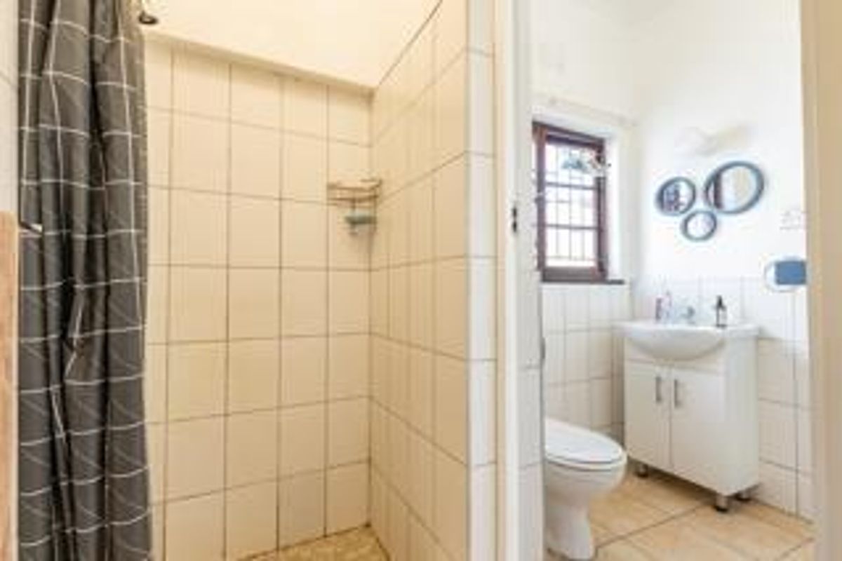 Functional bathroom featuring a shower with tiled walls, a vanity basin, and a toilet, with a window providing natural light.